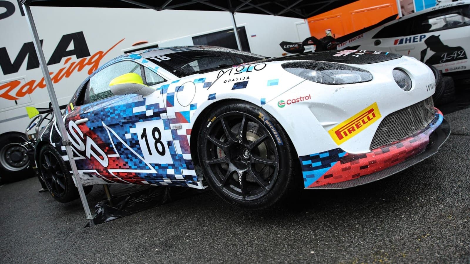 Ivan Pulić's white and blue Alpine A110 GT4, number 18, in the paddock in Saturday's rain, Nagrada Dubrovnika 2026.