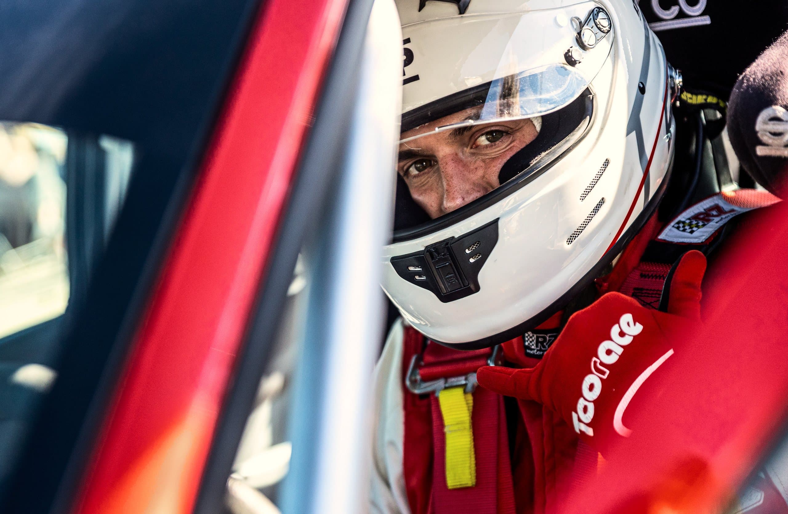 A driver in a white helmet, ready in a red car