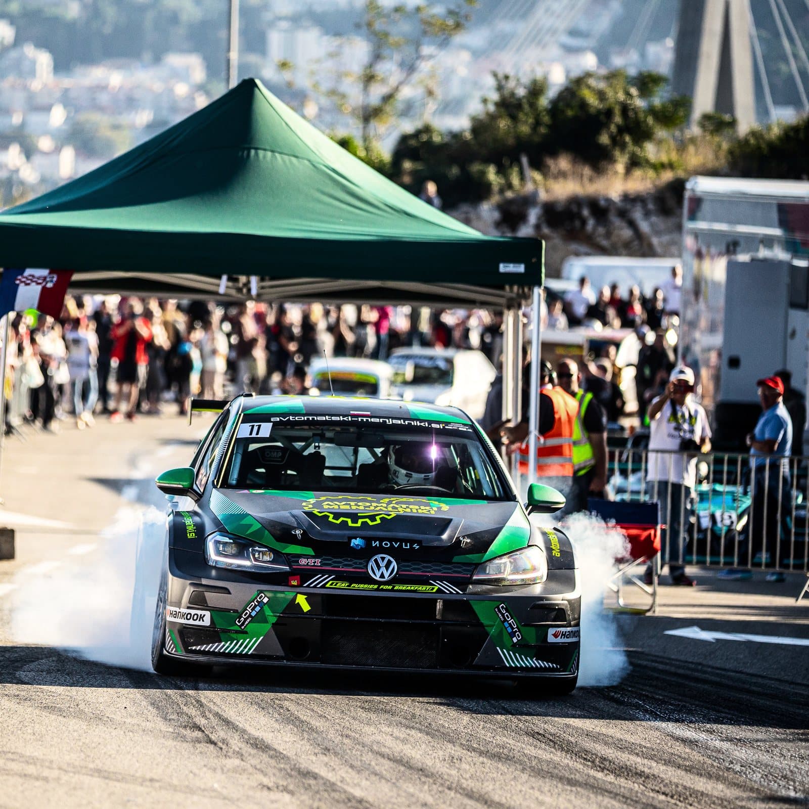 A green Volkswagen Golf spins its wheels at the start, the crowd behind it