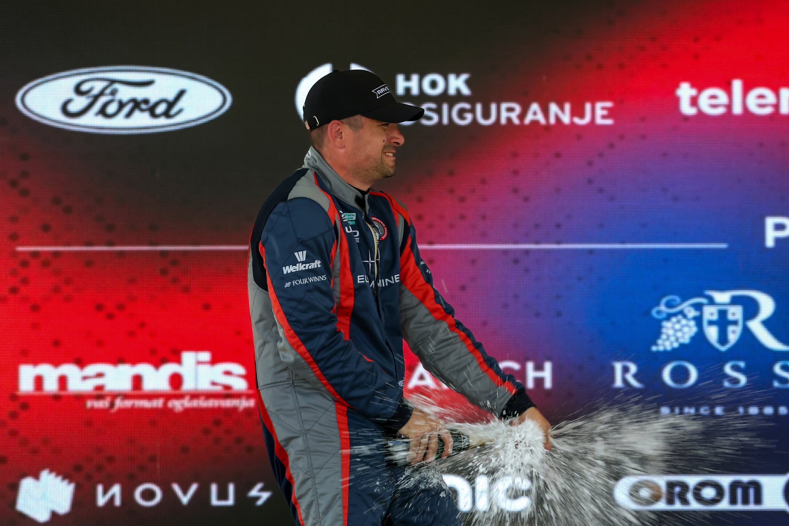 A driver sprays champagne on the podium in front of the partners' wall