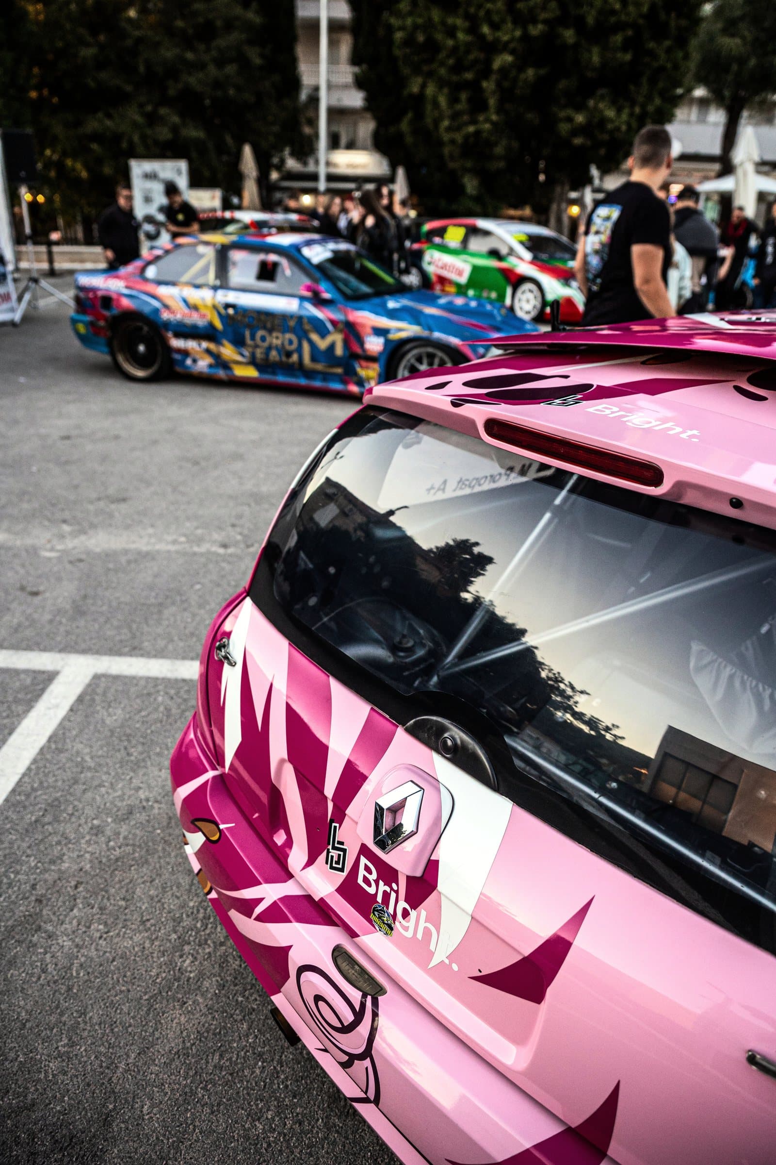 The pink Renault Clio from behind, with race cars and visitors in the Lapad car park